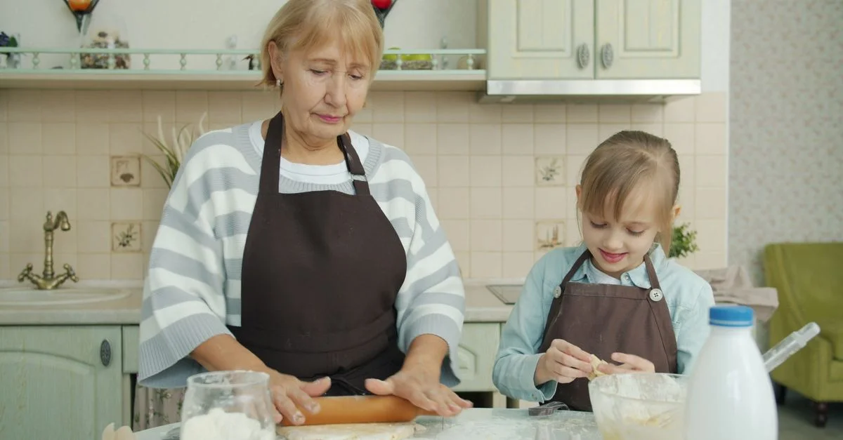 Une femme âgée et une jeune fille font de la pâtisserie ensemble, illustrant les liens familiaux et la cuisine à la maison.