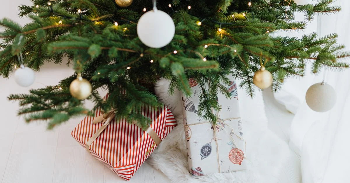 Scène de Noël chaleureuse avec un sapin décoré et des cadeaux emballés en dessous.