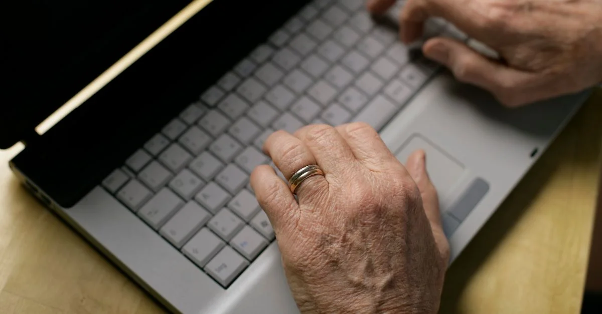 Gros plan sur des mains âgées tapant sur le clavier d'un ordinateur portable, mettant en avant l'utilisation de la technologie.