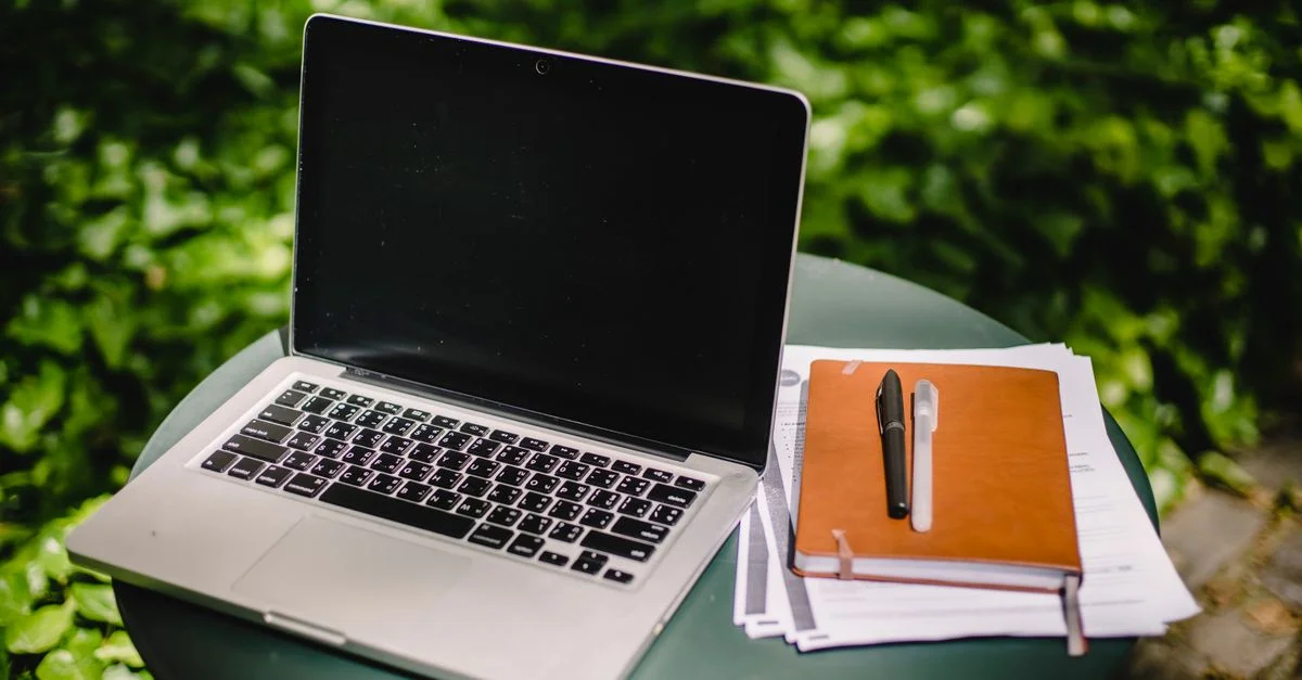 Ordinateur portable sur une table en extérieur avec un carnet et un stylo, espace de travail à distance idéal.