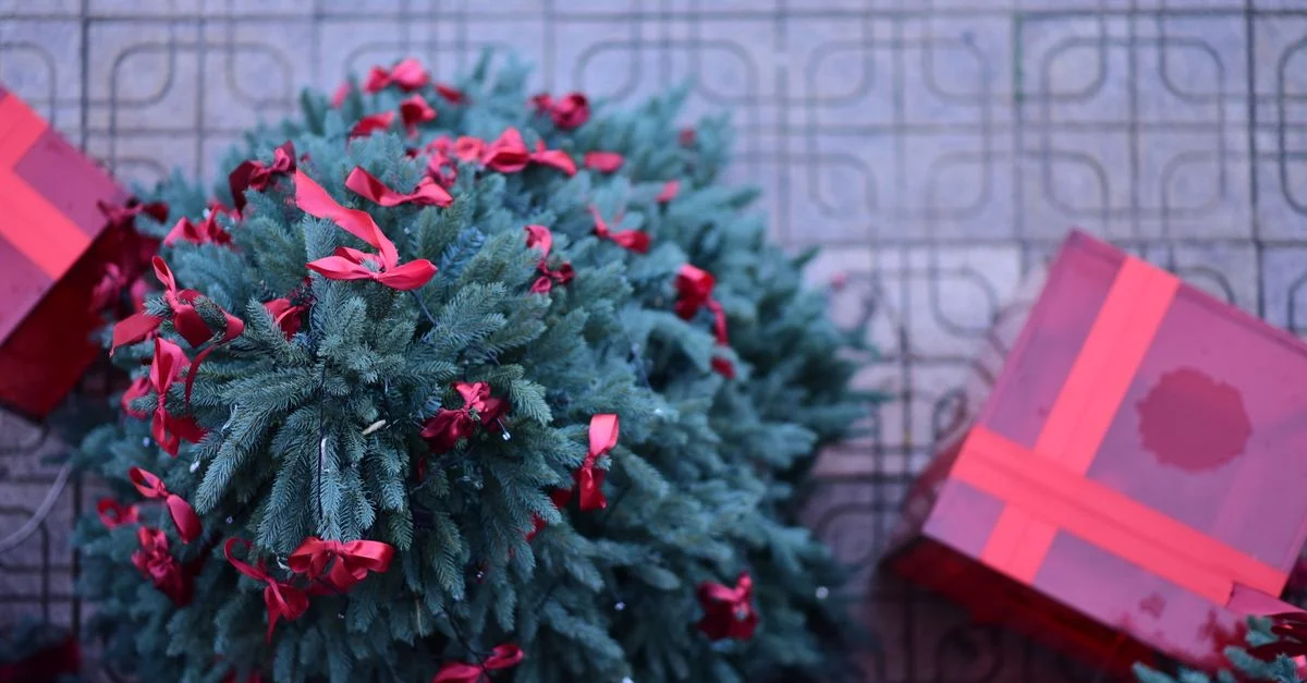 Arbre de Noël décoré de rubans rouges à côté de boîtes cadeaux emballées sur un sol carrelé extérieur.