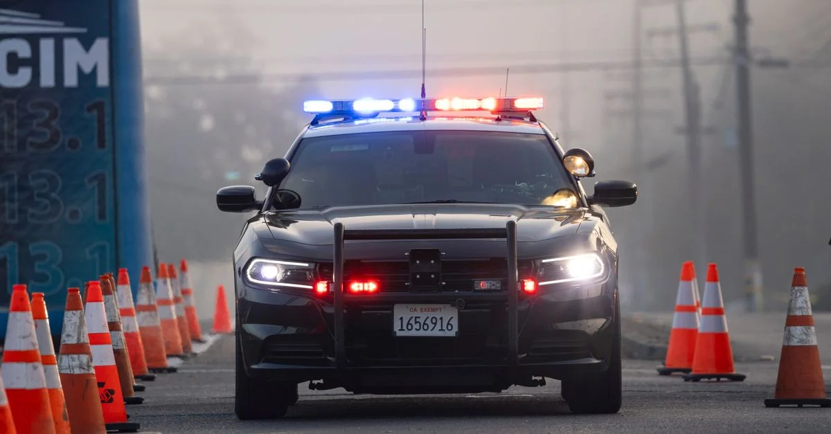 Une voiture de police avec des sirènes allumées à un point de contrôle routier entouré de cônes.