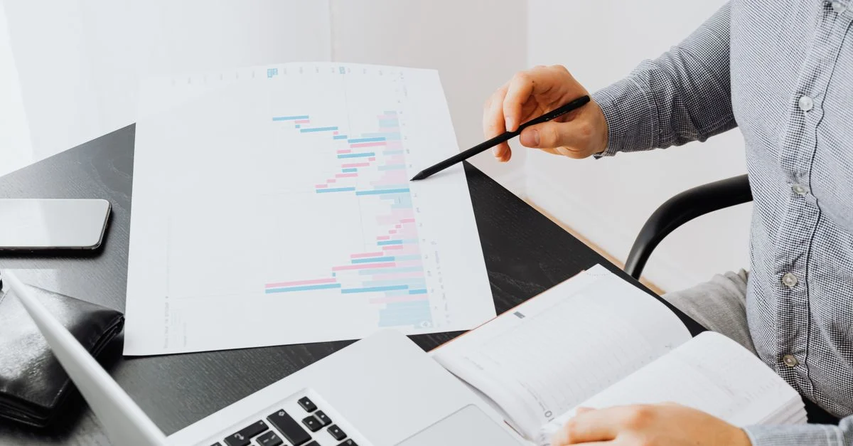 Un bureau avec une personne analysant une impression de graphique tout en utilisant un ordinateur portable et un carnet.