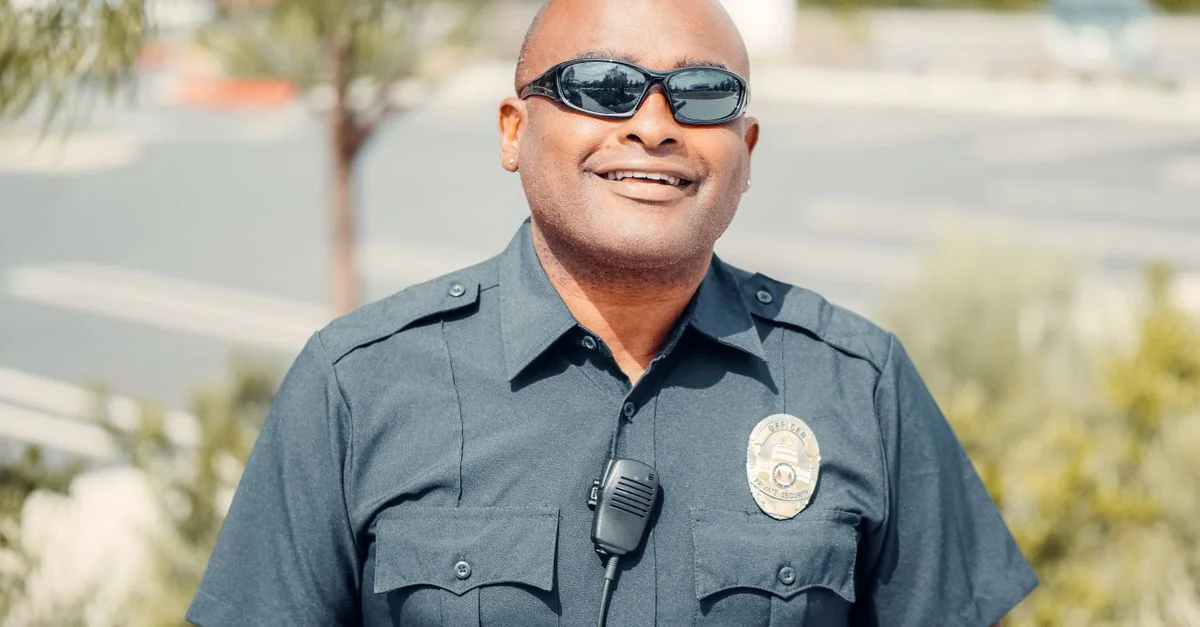 Portrait d'un policier souriant en extérieur portant des lunettes de soleil et un uniforme.
